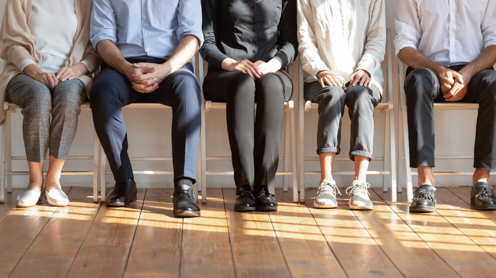 Diverse,People,Seated,On,Chairs,In,Row,Waiting,In,Queue